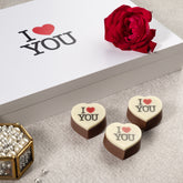 Heart-shaped chocolates with 'I ❤️ YOU' text, a red rose, and 'I ❤️ YOU' card on a textured surface.