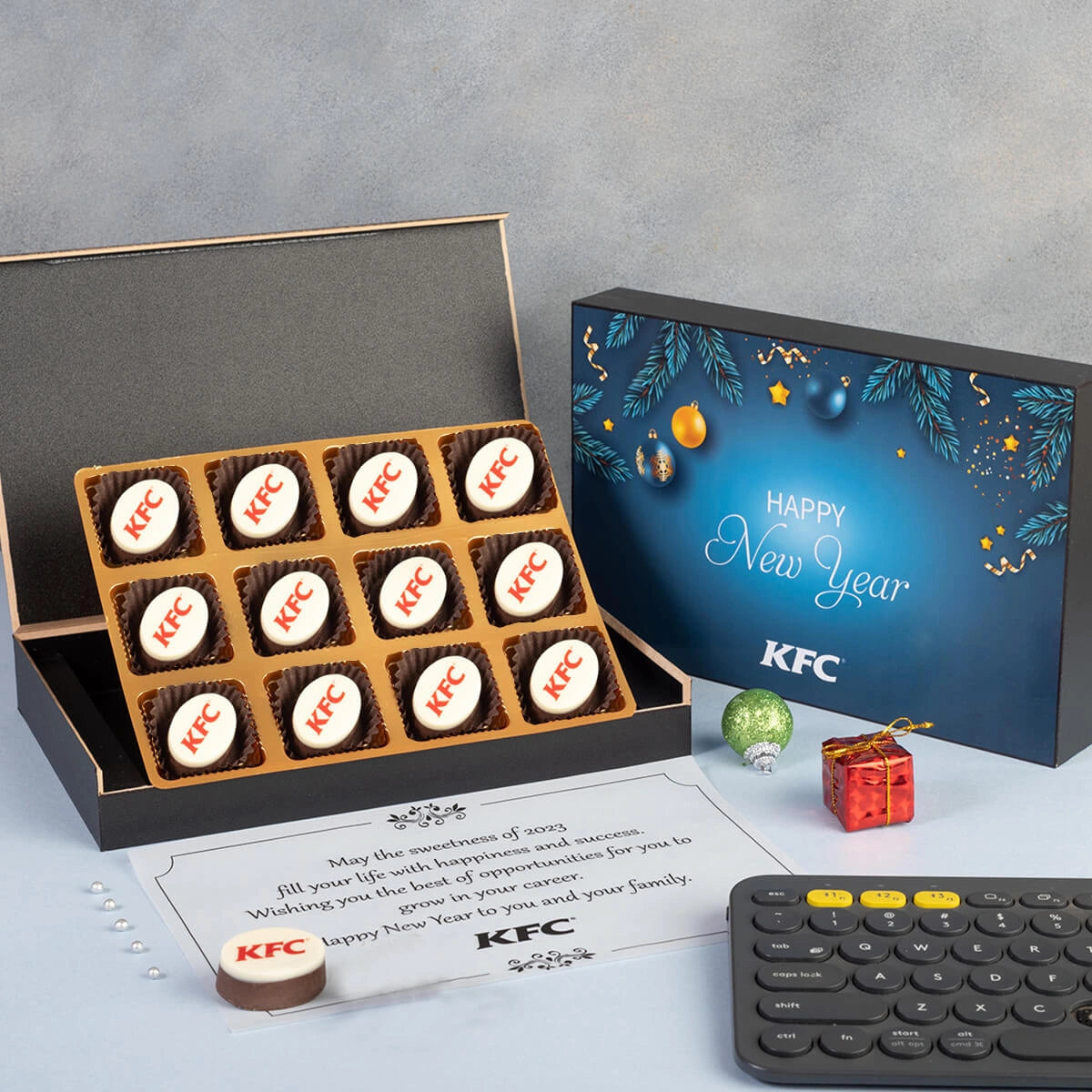 12‑piece New Year corporate gift box open to display mixed logo chocolates and festive packaging.